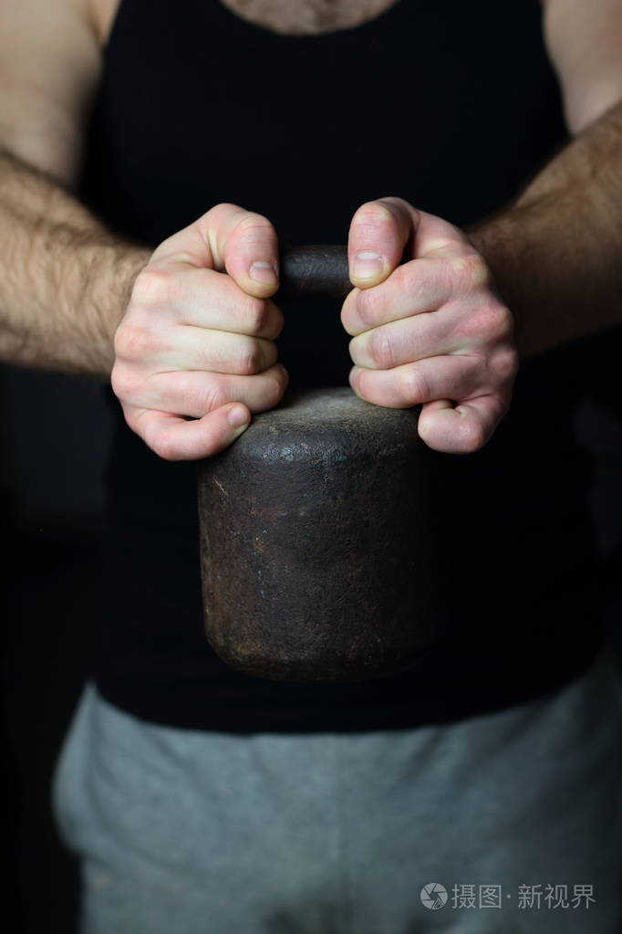 一个穿着黑色t恤和运动裤的男人粗暴地用强壮的双手握着一个老式的