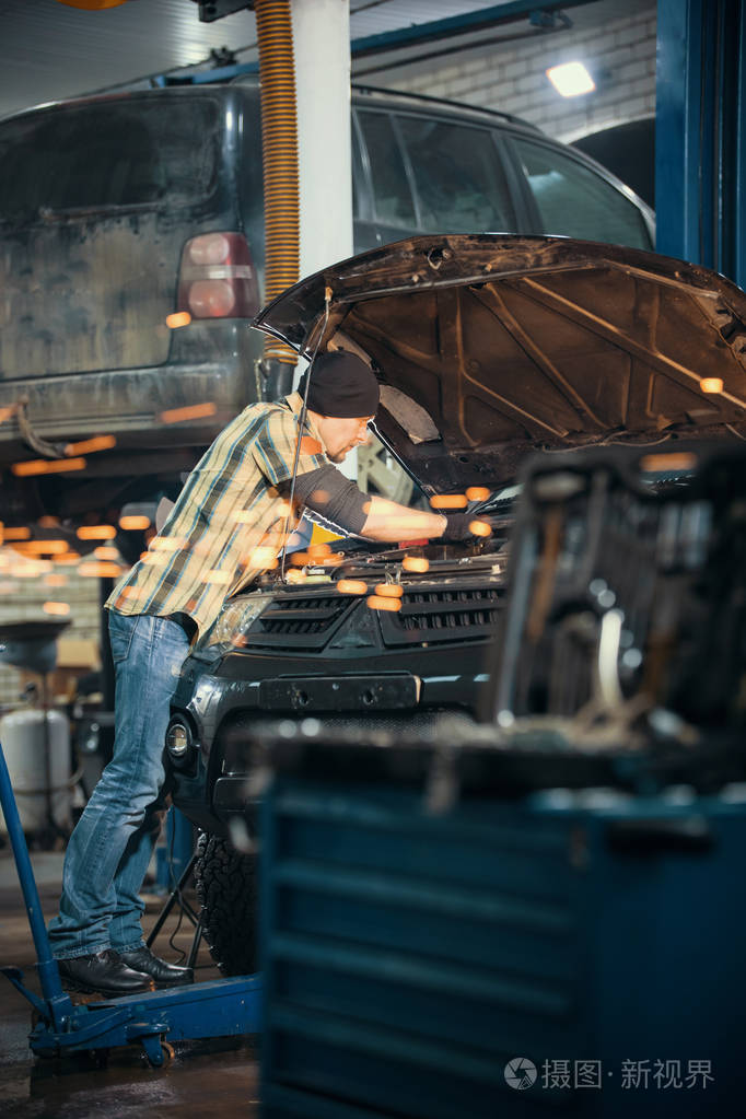 汽车维修服务.机械师站在车旁, 头戴敞篷, 做着自己的工作.火光