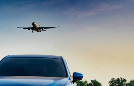 商业航空公司。客机降落接近蓝色SUV车在机场与蓝天和云彩在日落。抵达航班。休假时间。旅途愉快。飞机在明亮的天空上飞行。停着车。