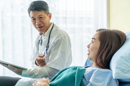 亚洲高级医生坐在病床上，与女性患者讨论选择性焦点