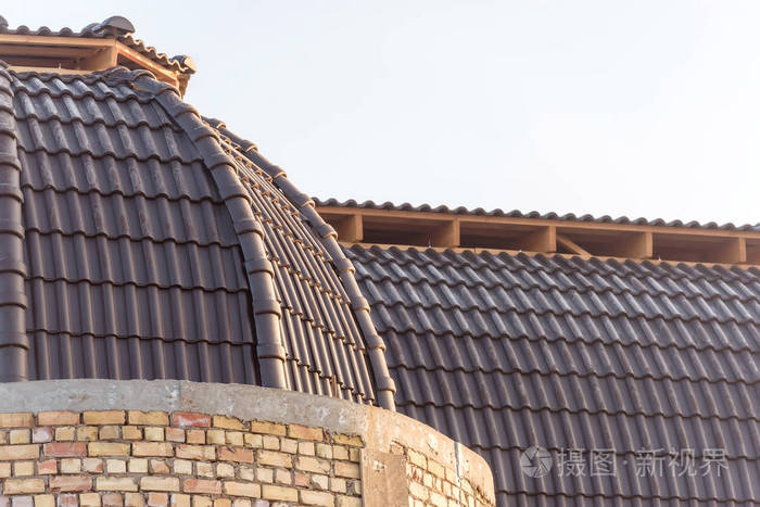 房子的圆顶被瓦片覆盖.深棕色的瓷砖.建筑.用砖头盖的房子.金属瓷砖.