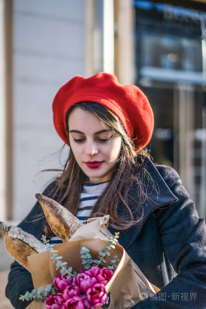 年轻漂亮的女法国女人,身穿红色贝雷帽和黑色外套,带着一束鲜花和法式