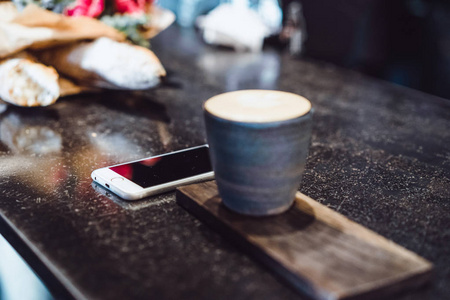 一个杯子，咖啡杯上放着咖啡卡布奇诺。智能手机，鲜花和卡布奇诺。桌子上的空间安排