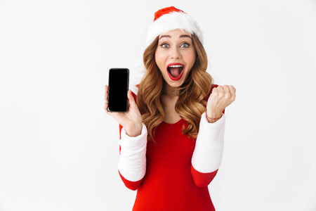 照片中一个震惊的情感女人穿着圣诞服装，展示手机，做赢家的手势。