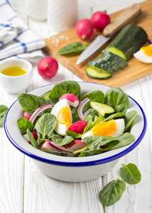 新鲜春季沙拉与菠菜，萝卜，黄瓜和鸡蛋。 美味的午餐健康食品夏季蔬菜。 在白色木制背景的碗里