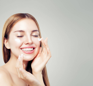 笑的女人，有健康的皮肤，在她的脸上涂上保湿霜。 护肤美容及面部护理概念