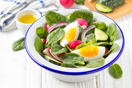 新鲜春季沙拉与菠菜，萝卜，黄瓜和鸡蛋。 美味的午餐健康食品夏季蔬菜。 在白色木制背景的碗里