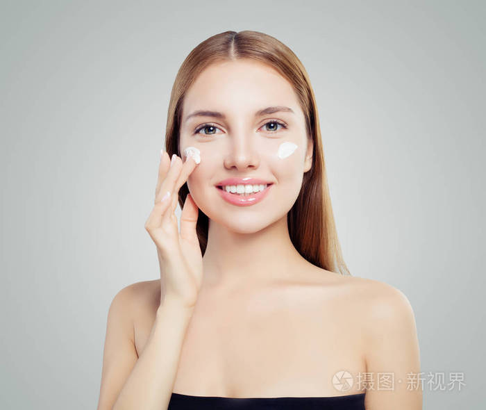 快乐美丽的女人在健康的皮肤上涂上奶油.