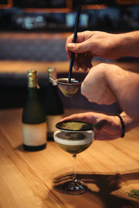 酒吧木桌上的筛制酒精鸡尾酒的调酒师的局部视图