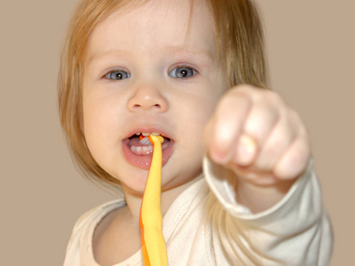 小宝贝女孩在学习刷牙的时候轻轻地玩，玩得很开心。 孩子用拇指在中指和食指之间显示拳头。