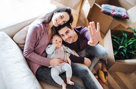 一对年轻夫妇带着一个婴儿和纸板箱搬到新家的画像