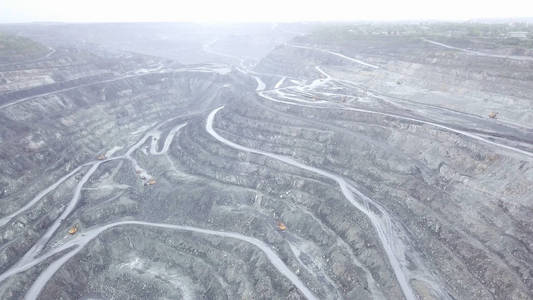 开放式采石场的顶部视图。与工作卡车一起在露天坑上站立灰色灰尘的全景。矿业理念