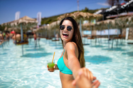 一幅年轻女子穿着比基尼在海滩上玩得开心微笑鸡尾酒的暑假肖像
