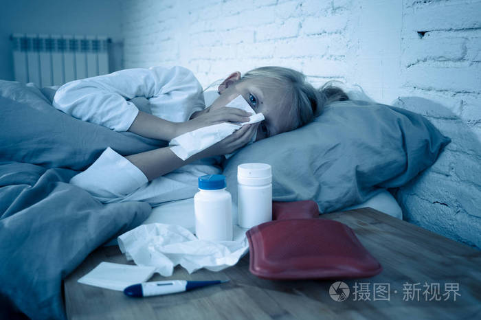 可爱的生病可爱的女孩生病躺在床上,拿着药,体温计,热水袋,患有感冒和