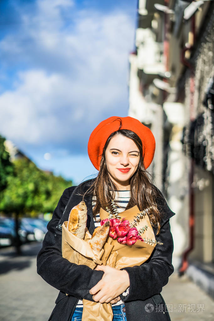 年轻漂亮的女法国女人身穿红色贝雷帽和黑色外套带着一束鲜花和法式小