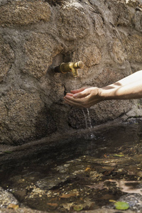 s hands picking fresh water from the spout of a stone fountain