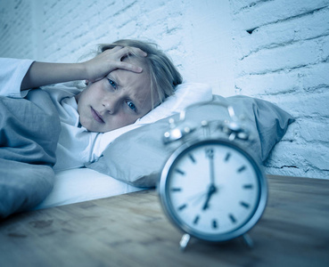 夜醒甜蜜的失眠小女孩躺在床上悲伤地看着闹钟,不得不醒来,但在烦恼中