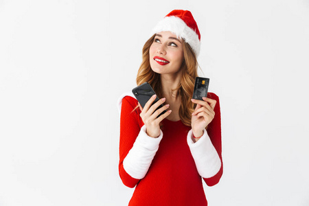 一个美丽的思考可爱的女人穿着圣诞服装，拿着信用卡和手机。
