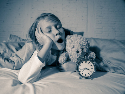 累趴下可爱可爱的失眠小女孩躺在床上,闹钟看起来很累,有睡眠问题