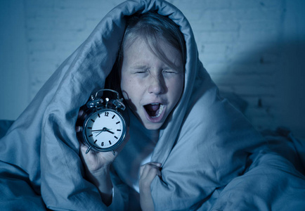 累趴下可爱可爱的失眠小女孩躺在床上,闹钟看起来很累,有睡眠问题