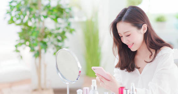 美丽的亚洲女人在家里化妆和使用智能手机