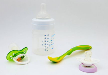 白色背景上的婴儿瓶和。 彩色婴儿勺子