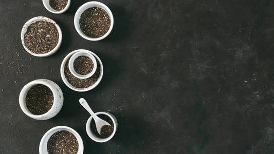 黑色桌面上的有机辣椒种子. 一套带有有机辣椒种子的小碗.