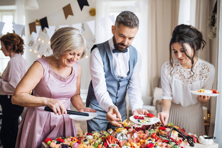 在室内家庭生日聚会上, 多代家庭将食物放在盘子里