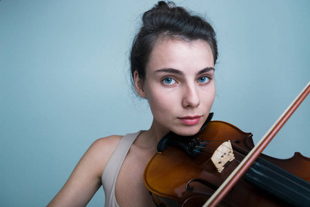 特写一位年轻漂亮的女士的肖像，她用小提琴摆姿势，被孤立在蓝色背景上