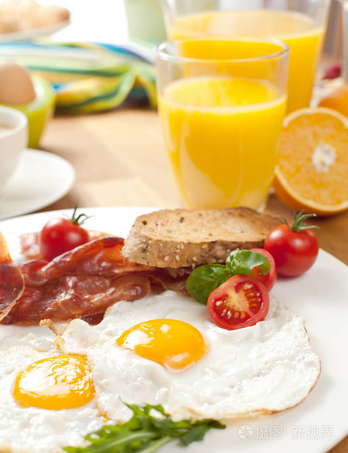 近距离观看美味的早餐，包括煎鸡蛋和培根樱桃西红柿橘子和果汁。