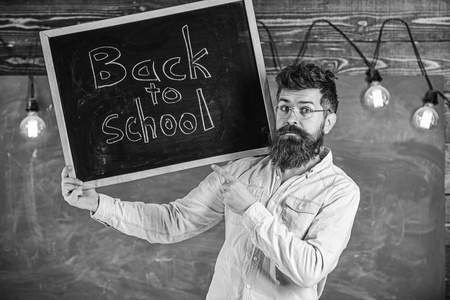 戴眼镜的老师把黑板和标题放回学校。高中的概念。胡子和胡子的人在严密的面孔欢迎学生, 黑板在背景上