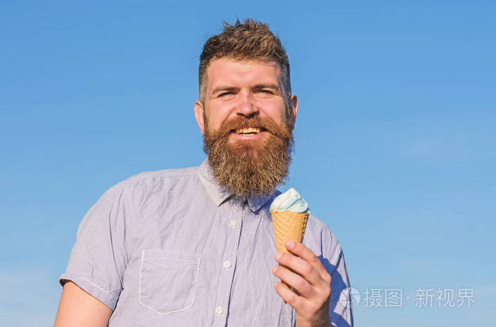 长胡子的人喜欢冰淇淋。甜食概念。男人用胡子和胡子在笑脸上吃冰淇淋, 蓝天背景, 弥散。有胡子的人与冰淇淋锥体