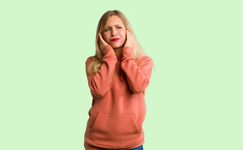 年轻女孩用手捂住耳朵。 绿色背景下沮丧的表情