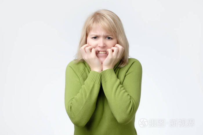 穿着绿色毛衣的女人害怕, 害怕和焦虑咬她的指甲, 看着相机照片-正版