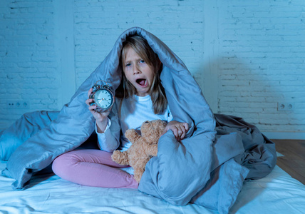 可爱的失眠小女孩坐在床上，看着悲伤和疲惫，有睡眠问题，晚上睡觉，或者凌晨醒来太早，失眠焦虑睡眠障碍的儿童。
