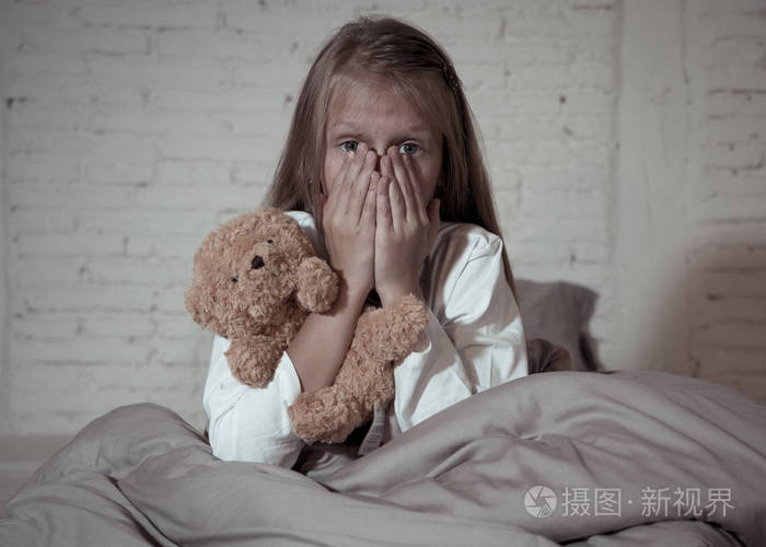 害怕的小女孩坐在床上用手抱着她的泰迪害怕黑暗中的怪物在卧室里孩子