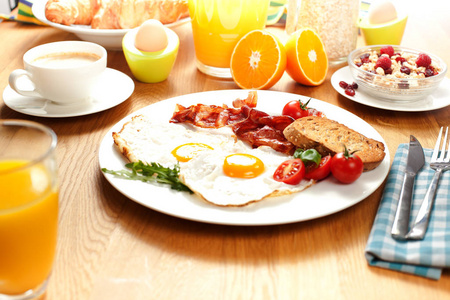 煎蛋与培根和西红柿，橙汁，咖啡，梅斯利与浆果，煮鸡蛋和牛角面包在木桌上