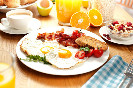 提供煎鸡蛋培根和西红柿橙汁咖啡浆果酱煮鸡蛋和牛角面包，早餐放在木桌上