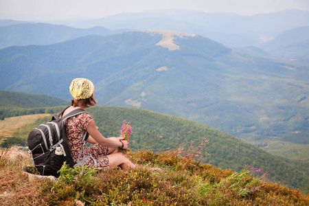 旅游妇女带背包，穿着夏装，鲜花欣赏山景。 在山里跋涉