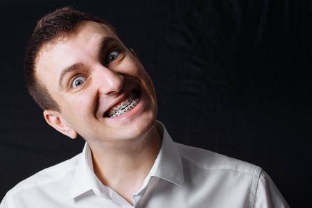 一个白种人的肖像，他的牙齿上戴着一件黑色背景的白色衬衫，牙齿上戴着金属支架。 牙学概念牙齿矫正学医学定位