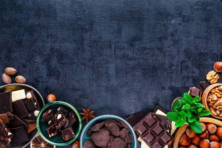 巧克力块的灰色背景可可粉和各种坚果和香料碗的顶部视图。 糖果店广告。