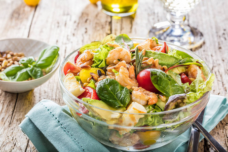在木制桌子上的玻璃碗里放新鲜蔬菜和虾，近距离观看美食沙拉