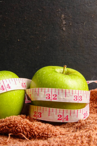 健康生活方式的概念绿色苹果和测量磁带在黑色的乡村背景。 选择性聚焦。