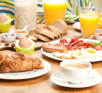 美味的早餐，新鲜美味的牛角面包，煎鸡蛋，培根，果汁，咖啡和切片面包，提供在桌子上。