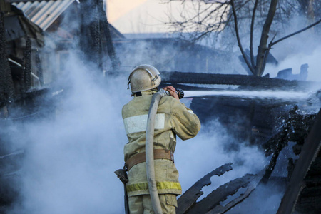 消防员灭火。 消防员拿着软管浇水，浓烟中燃烧的木结构。