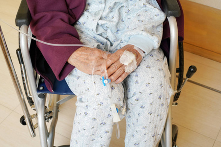 医院轮椅上静脉滴注的老年女性双手并拢