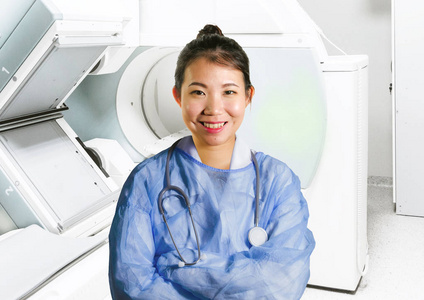 年轻快乐有魅力的亚洲中医女医生，穿着蓝色的工作服，在医院的扫描仪室，在医疗保健和成功的医疗职业理念中微笑，开朗