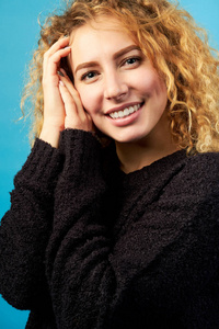 年轻迷人微笑开朗卷曲的姜姑娘穿着黑色毛衣的肖像。在蓝色背景上拍摄的工作室。