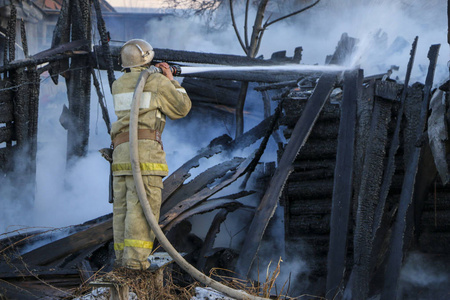 消防员拿着软管浇水,浓烟中燃烧的木结构.照片