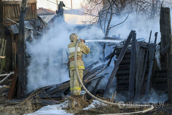 消防员拿着软管浇水,浓烟中燃烧的木结构.